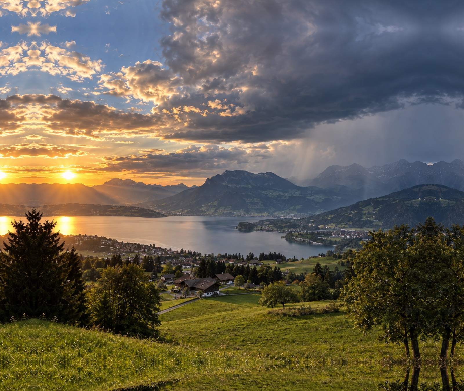 Schweizer Voralpenlandschaft mit See, grünen Hängen, Sonne und einzelnen dunkleren Wolken