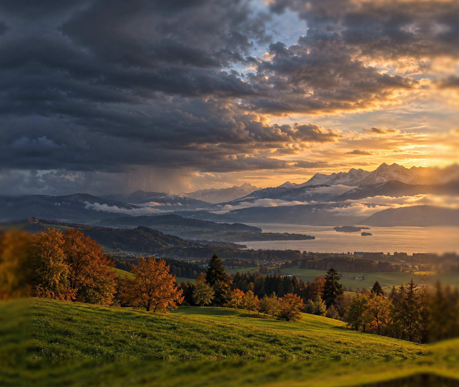 Schweizer Herbstlandschaft mit dunklen Wolken im Westen und Abendsonne über See und Alpen