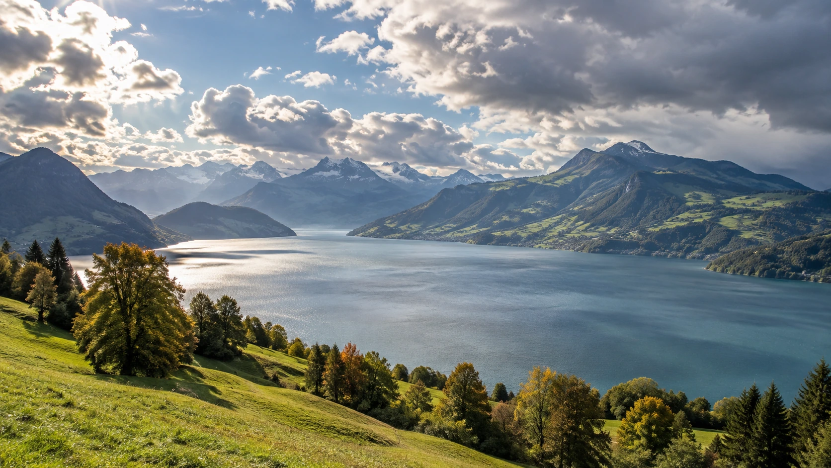 Sonnige Schweizer Landschaft mit See und Alpen unter wechselnden Wolken.