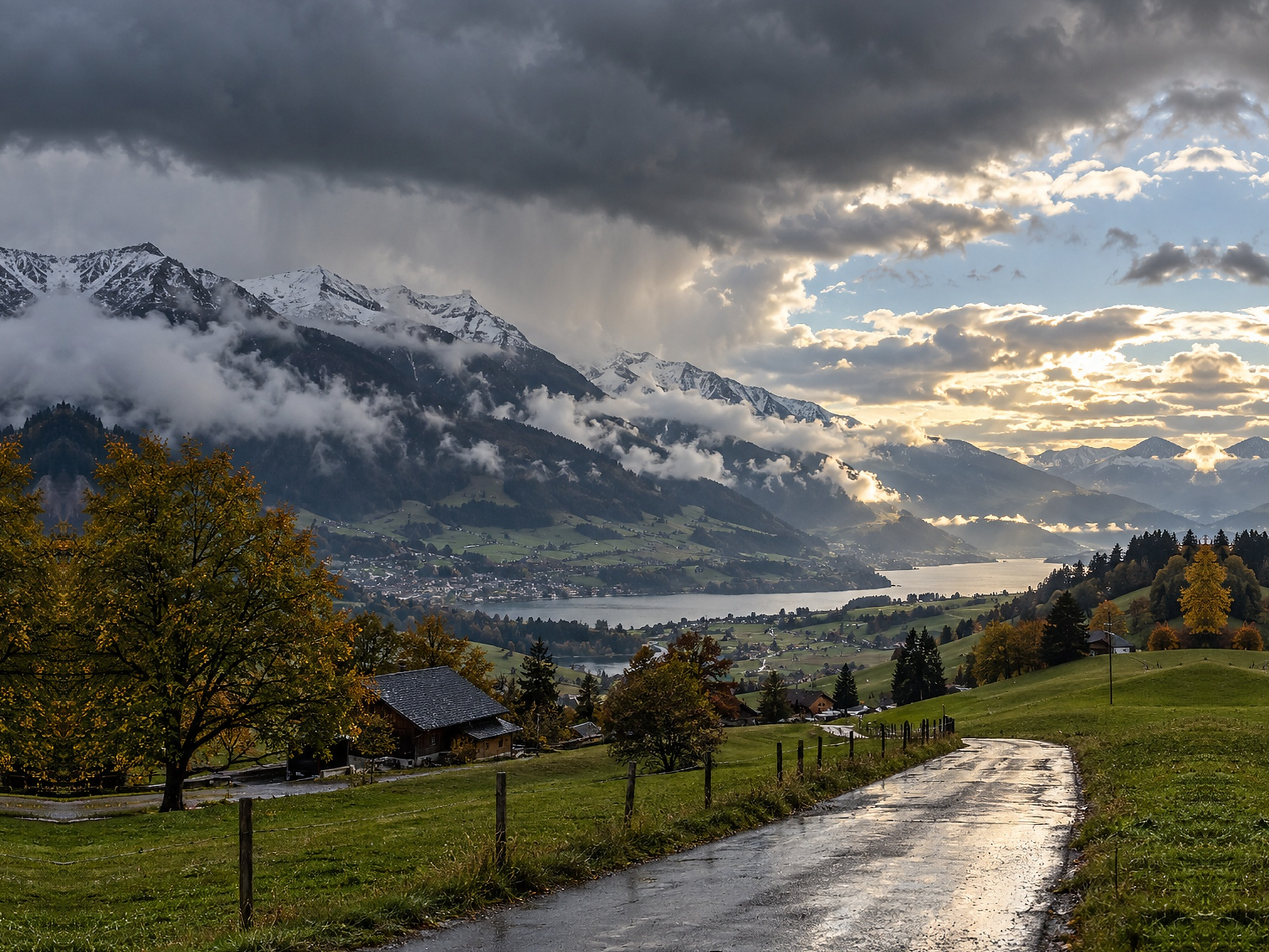 Wechselhaftes Septemberwetter in einer Schweizer Berglandschaft mit nasser Strasse, Wolken und Aufhellungen