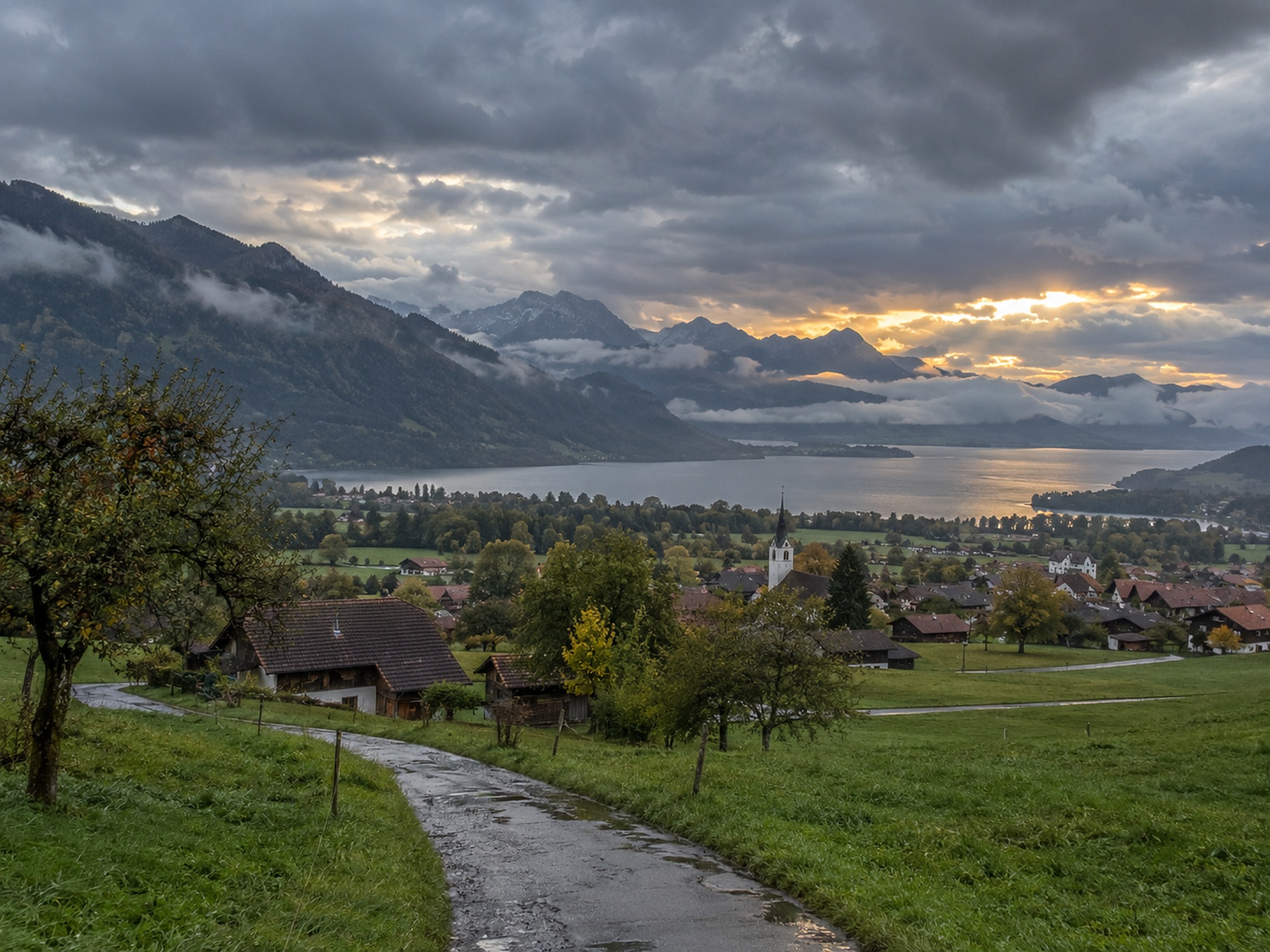 Wechselhaftes Abendwetter über einer Schweizer Seenlandschaft mit Dorf und Bergen