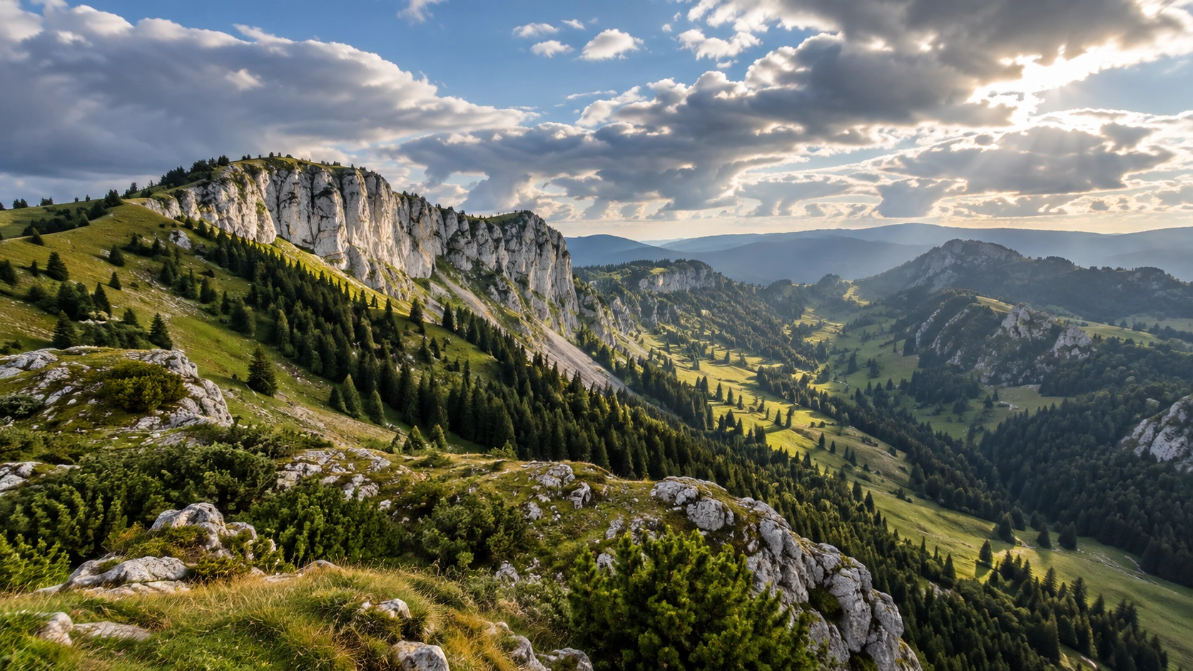 Weite Schweizer Jura- und Voralpenlandschaft mit Kalkfelsen, grünen Hängen und aufgelockerter Bewölkung.