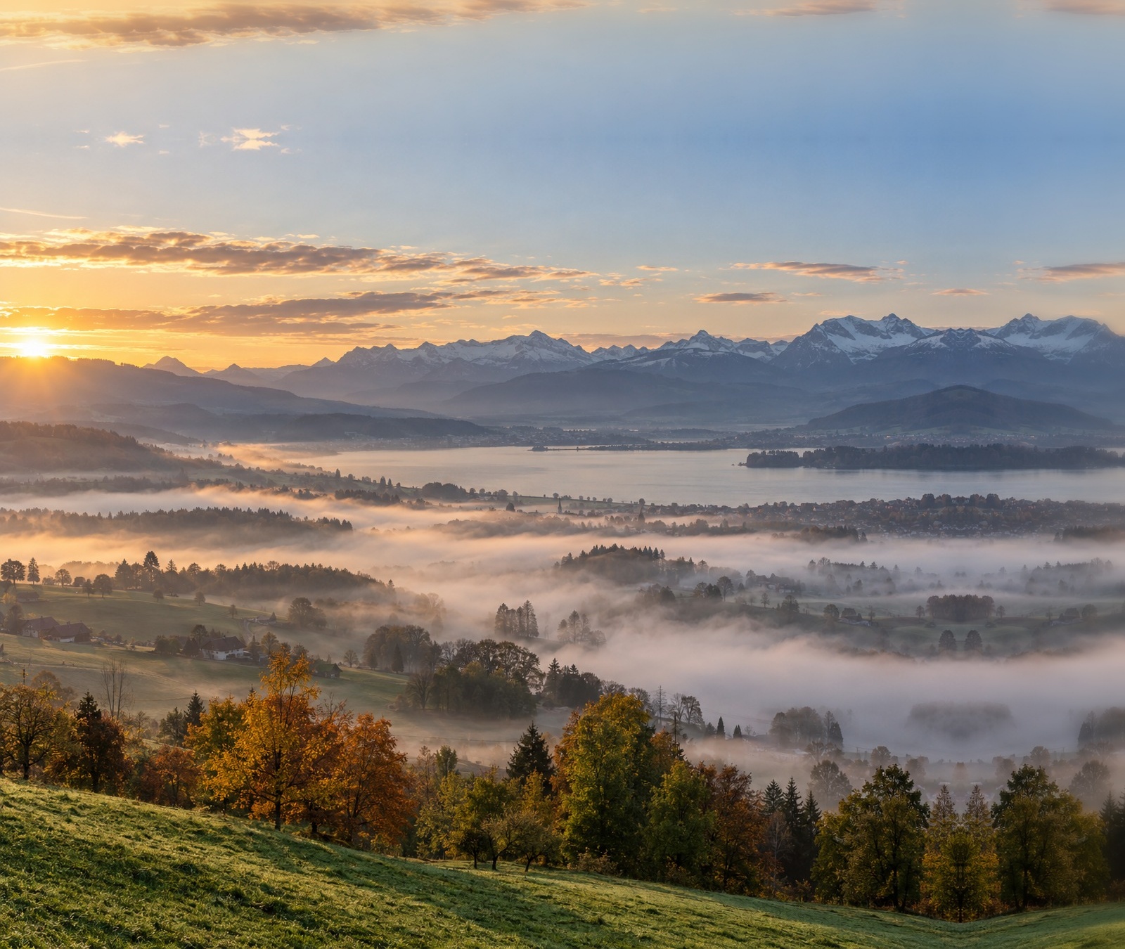 Herbstliche Schweizer Seen- und Alpenlandschaft mit Nebelfeldern und freundlicher Morgenstimmung als Symbolbild für das Tageswetter.