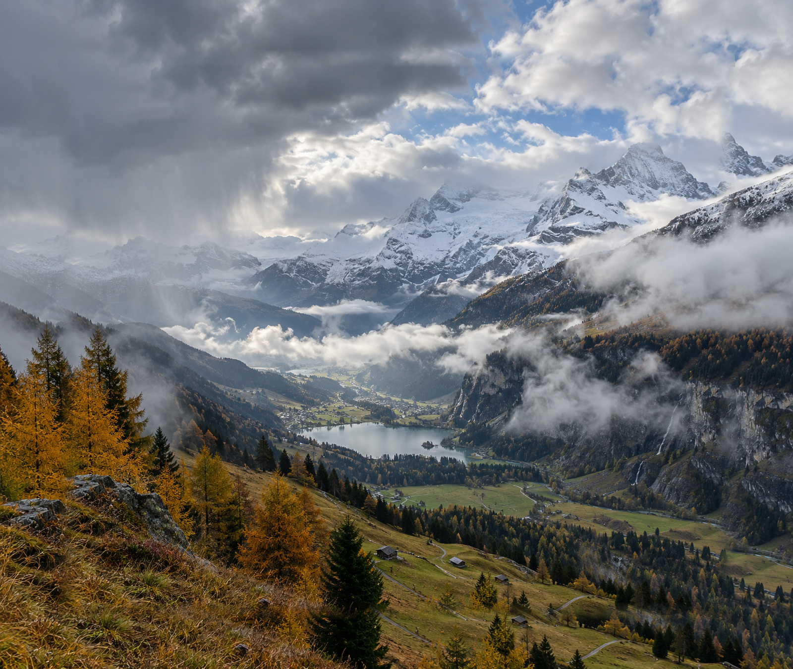 Herbstliche Schweizer Alpenlandschaft unter einer heranziehenden Kaltfront mit Regenwolken und frischem Schnee in den Hochlagen.