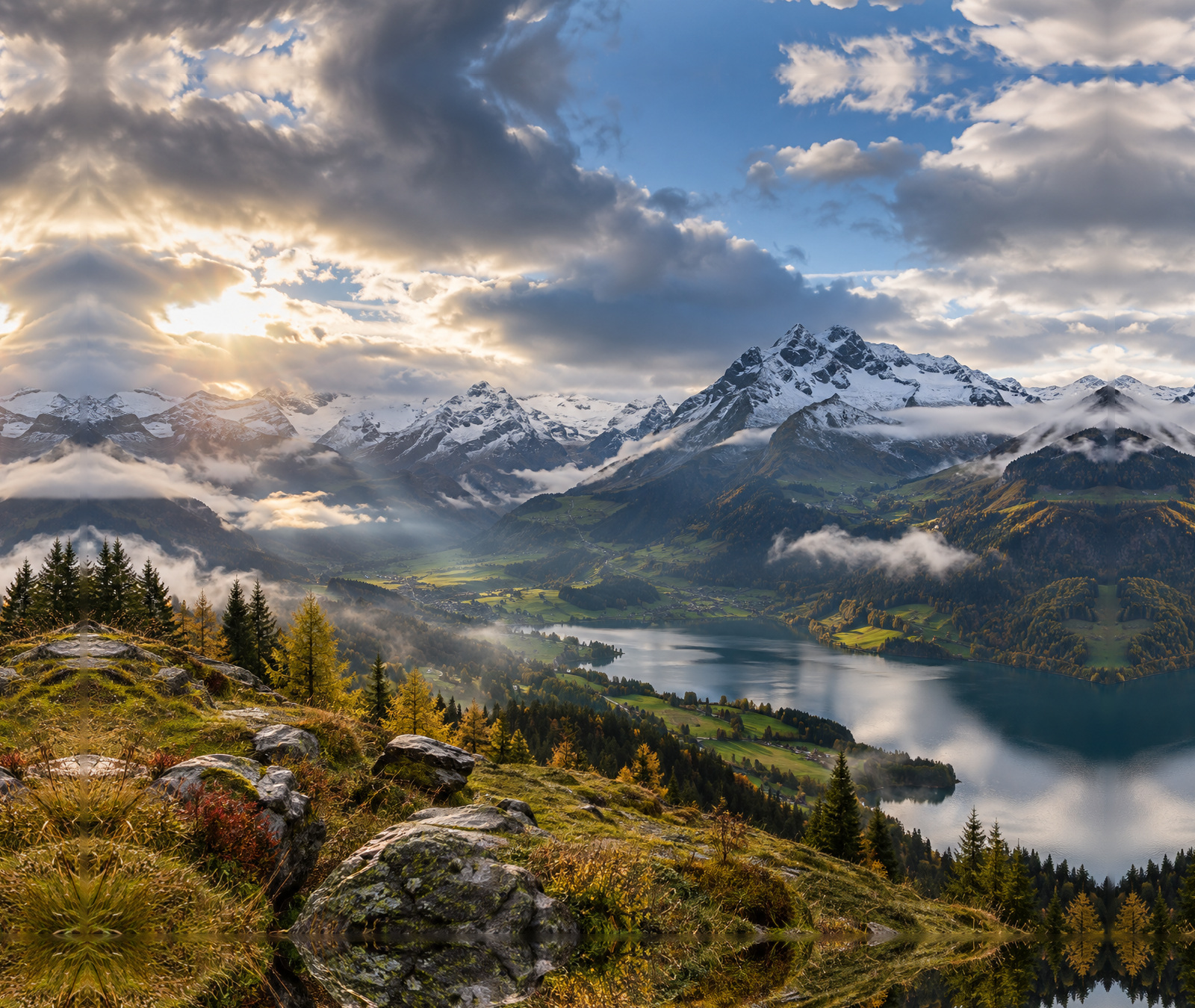 Herbstliche Schweizer Alpenlandschaft mit Wolkenfeldern, sonnigen Abschnitten und verschneiten Hochgipfeln